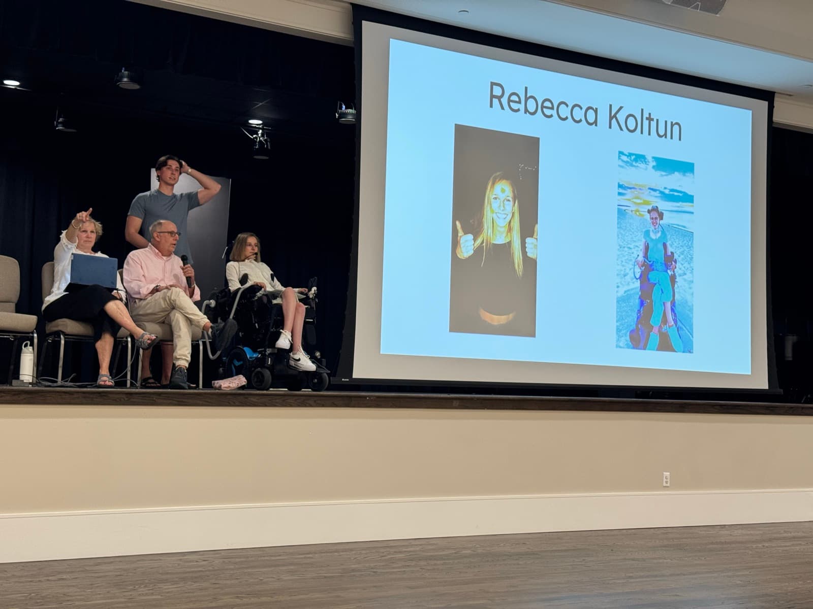 Rebecca and her family on the Valencia stage next to a projected slide reading “Rebecca Koltun”.
