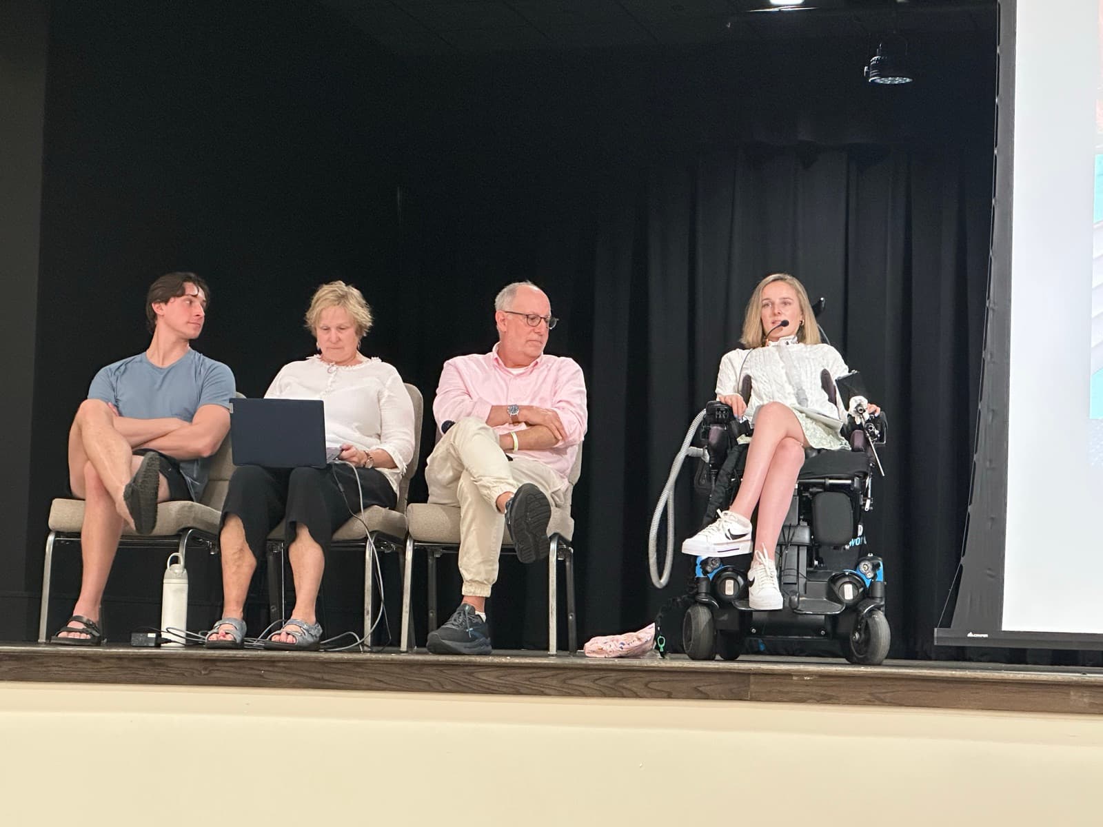 Rebecca on a big stage in her wheelchair alongside her family during a panel talk at the Valencia living community.